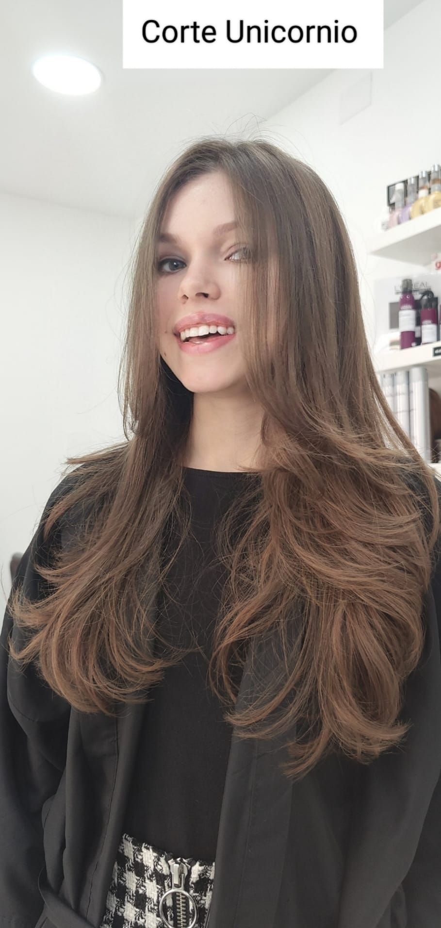 Una mujer con cabello largo y castaño lleva un abrigo negro y sonríe.