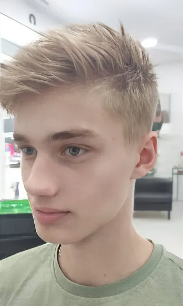 Un joven de cabello rubio lleva una camisa verde y mira a la cámara.