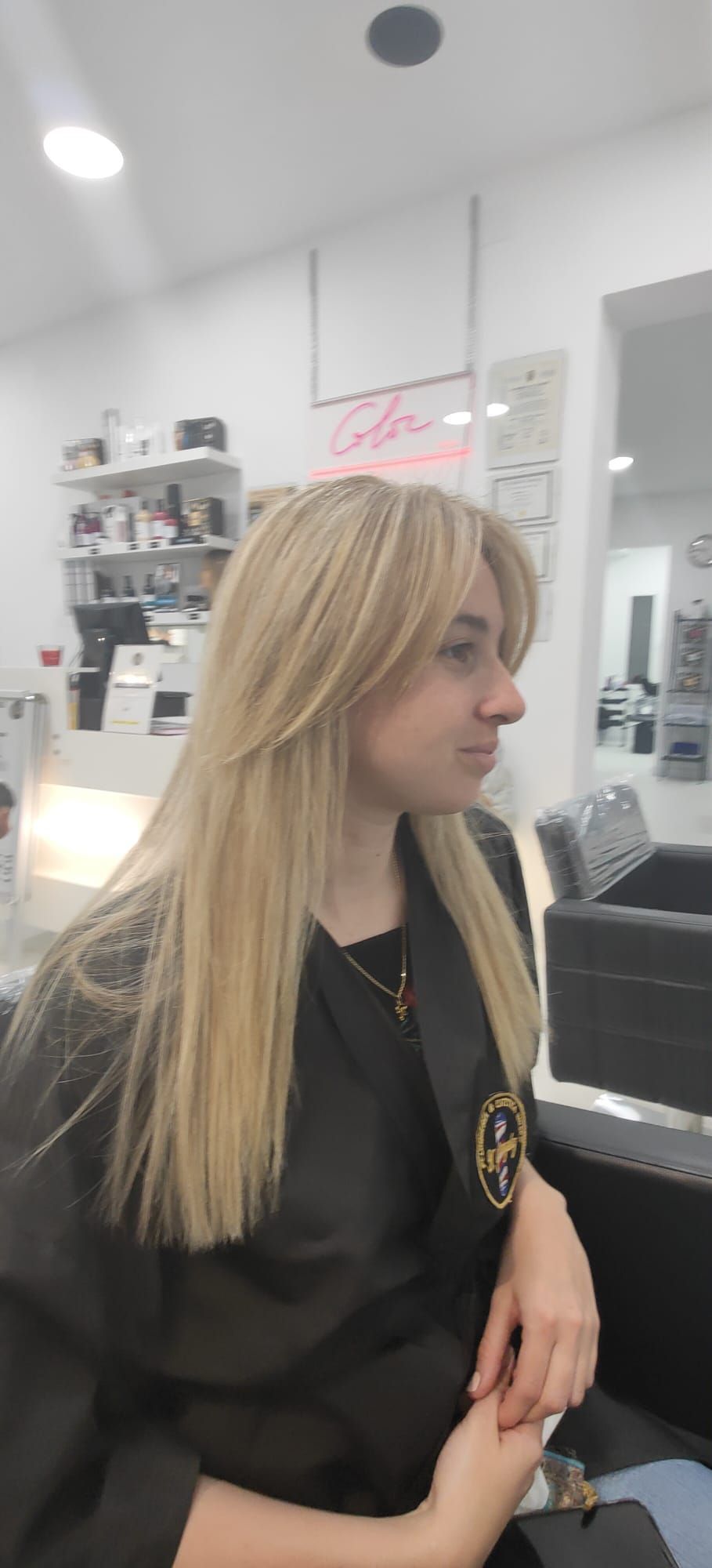 Una mujer con cabello largo y rubio está sentada en una silla en un salón.