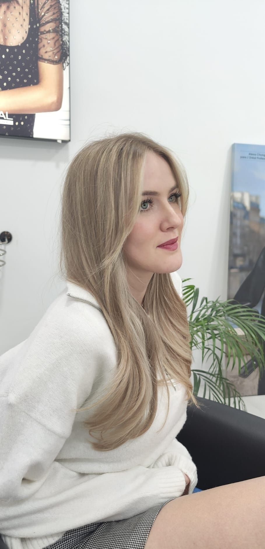 Una mujer con cabello largo y rubio está sentada en una silla en una habitación.
