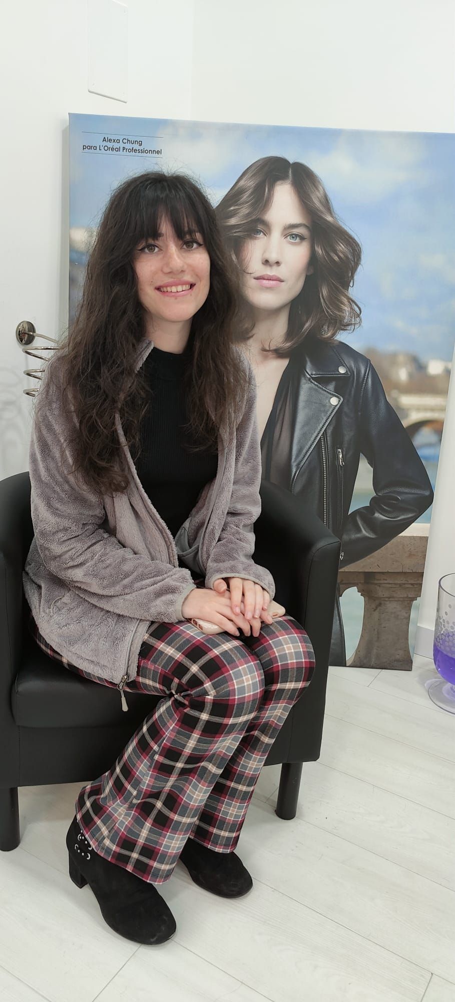 Una mujer está sentada en una silla al lado de un cuadro de una mujer.