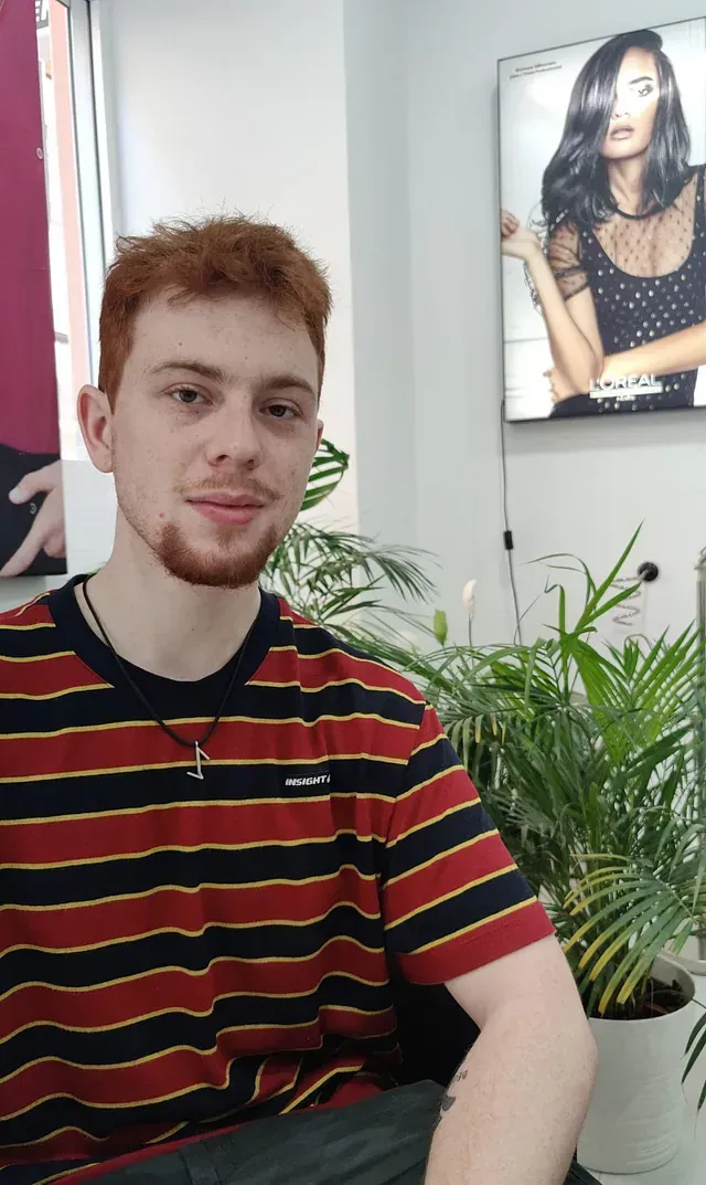 Un joven con una camisa a rayas está sentado delante de una planta en maceta.