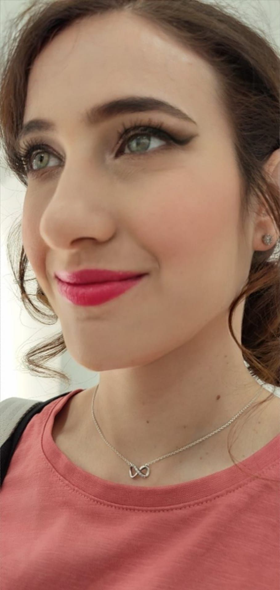 Un primer plano del rostro de una mujer que lleva una camisa rosa y un collar.