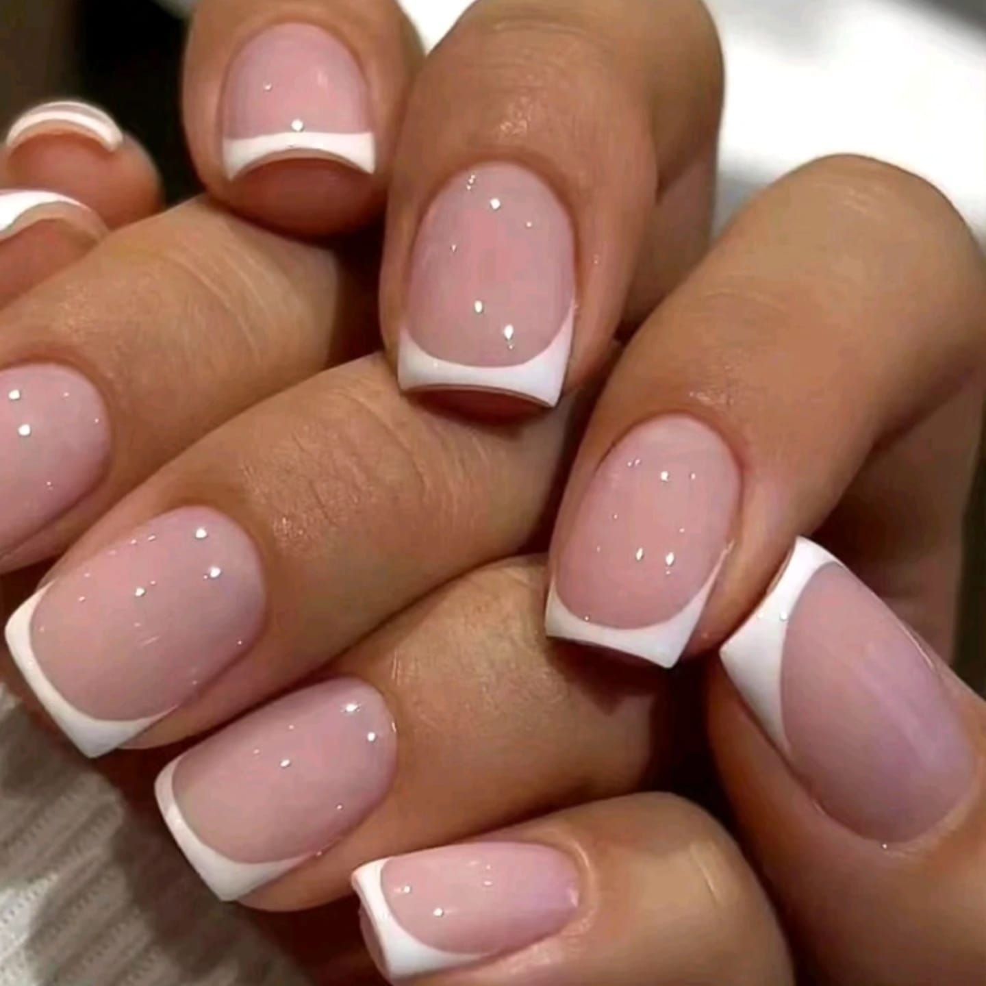 Un primer plano de las uñas de una mujer con una manicura francesa blanca.