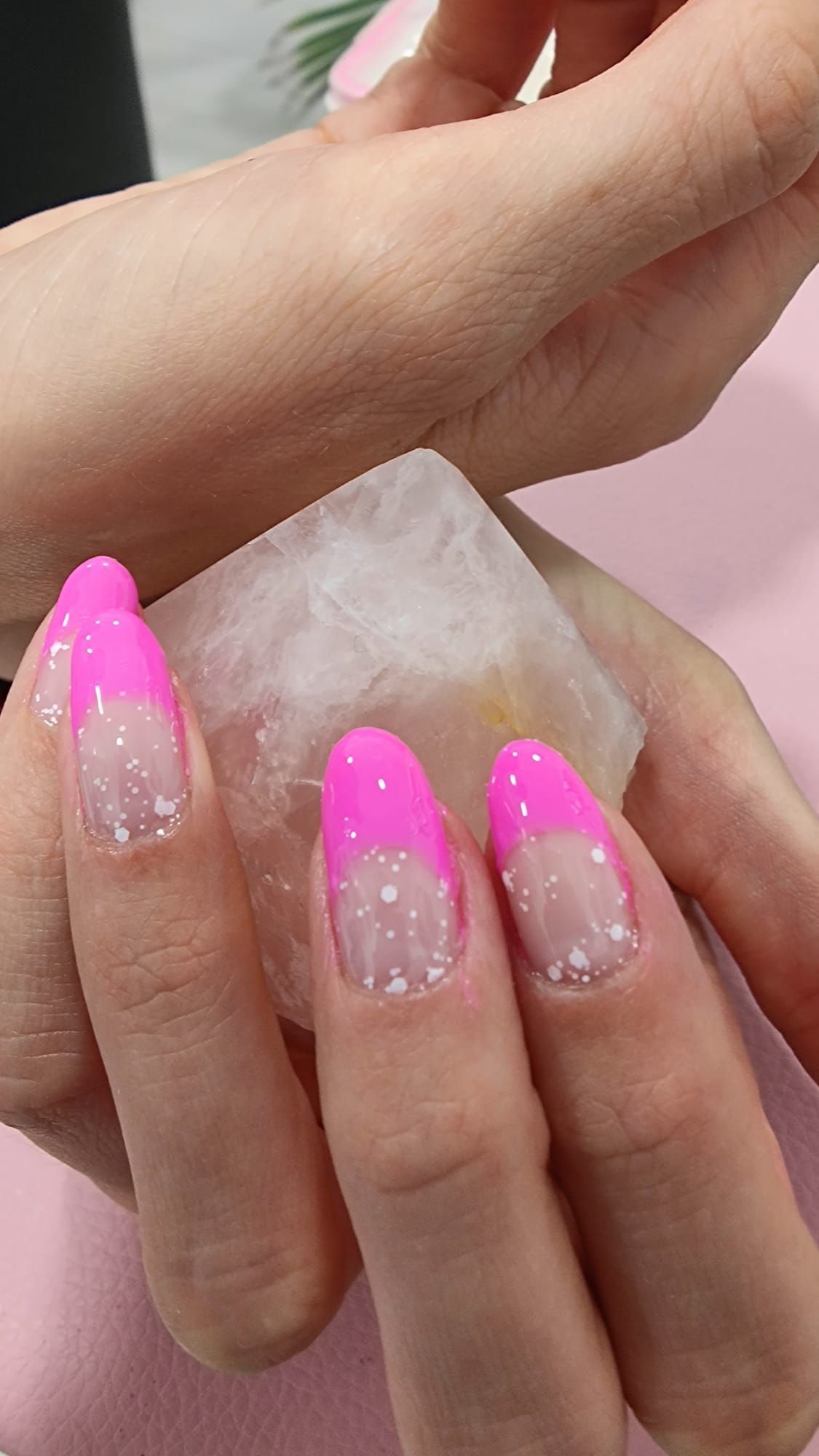 Un primer plano de las manos de una persona con uñas rosadas sosteniendo un trozo de hielo.