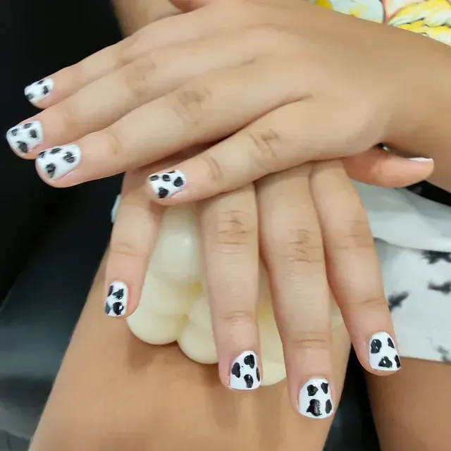 Un primer plano de las manos de una persona con uñas con estampado de vaca.
