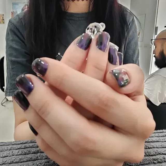 Una mujer con uñas moradas sostiene un osito de peluche en sus manos.