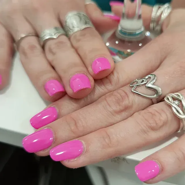 Un primer plano de las manos de una mujer con uñas rosas y anillos plateados.
