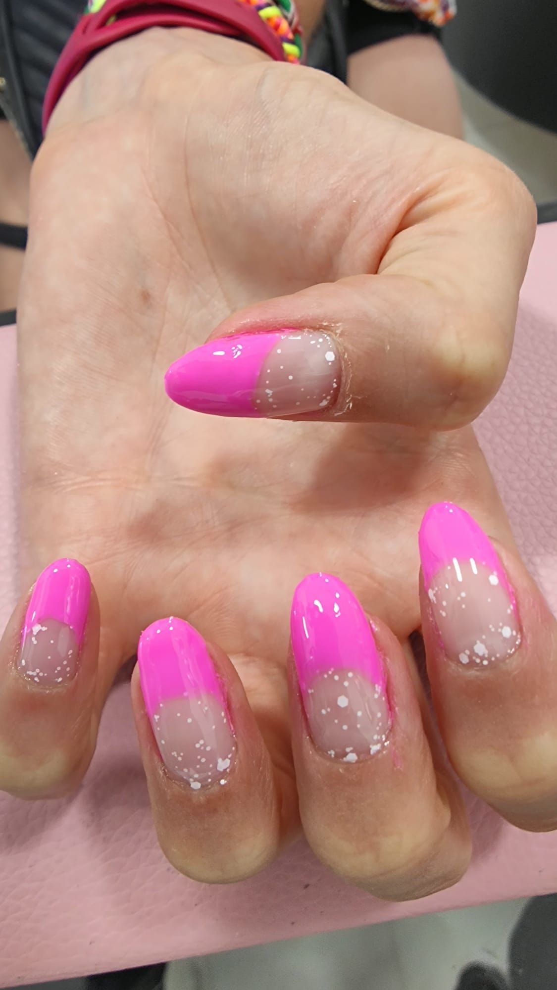 Un primer plano de la mano de una persona con uñas rosadas y blancas.