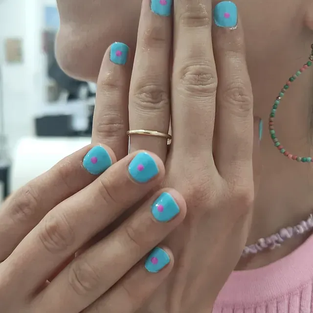 Un primer plano de las manos de una mujer con uñas azules y puntos rosados