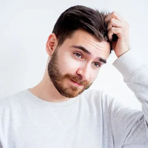 Un hombre con barba se rasca la cabeza.