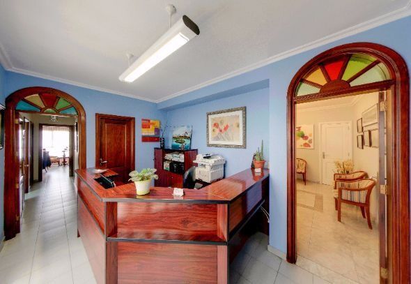 Vestíbulo de oficina luminoso con paredes azules, mostrador de recepción de madera y puertas arqueadas que dan a las habitaciones.