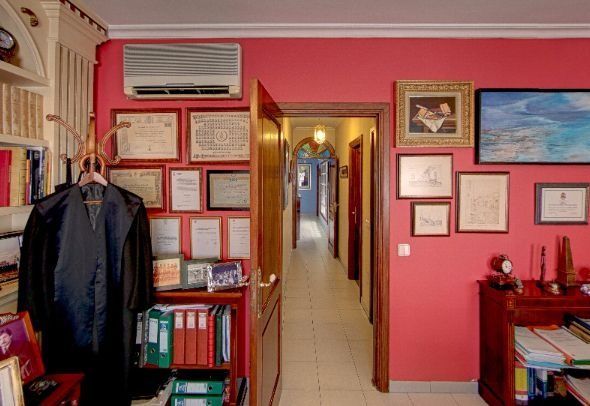 Pasillo de oficina pequeño con paredes rojas, certificados enmarcados, un perchero y una pintura abstracta azul.