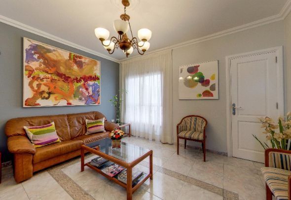 Sala de estar luminosa con sofá naranja, mesa de centro de cristal, coloridos cuadros en la pared y puerta blanca.