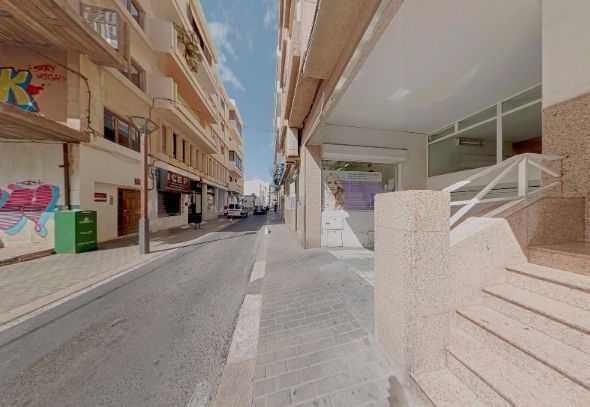 Calle estrecha y soleada entre edificios de apartamentos con una escalera y una acera en primer plano.