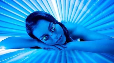 Mujer tumbada y relajada en una cama de bronceado azul, con gafas y rodeada de una intensa luz azul
