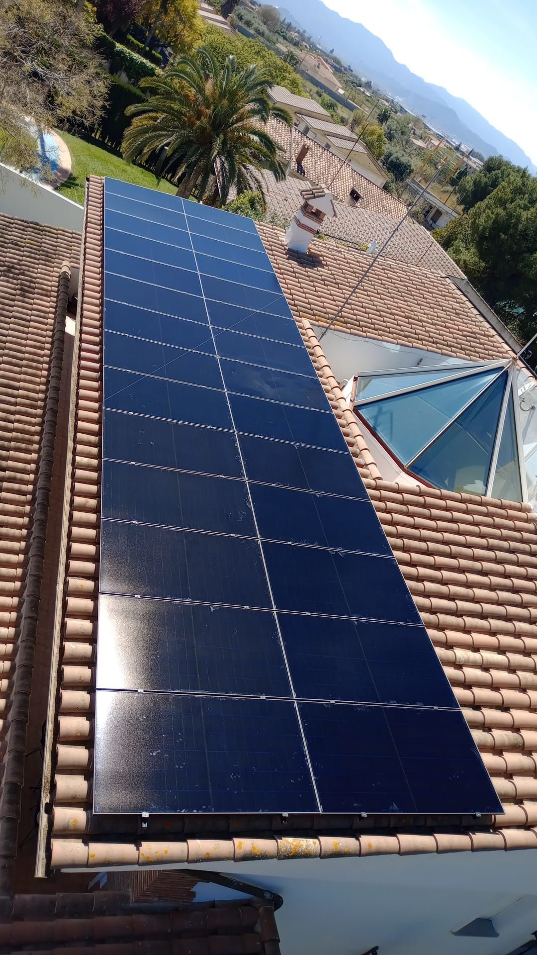 Paneles solares instalados en un techo de tejas rojas, en un entorno exterior soleado.