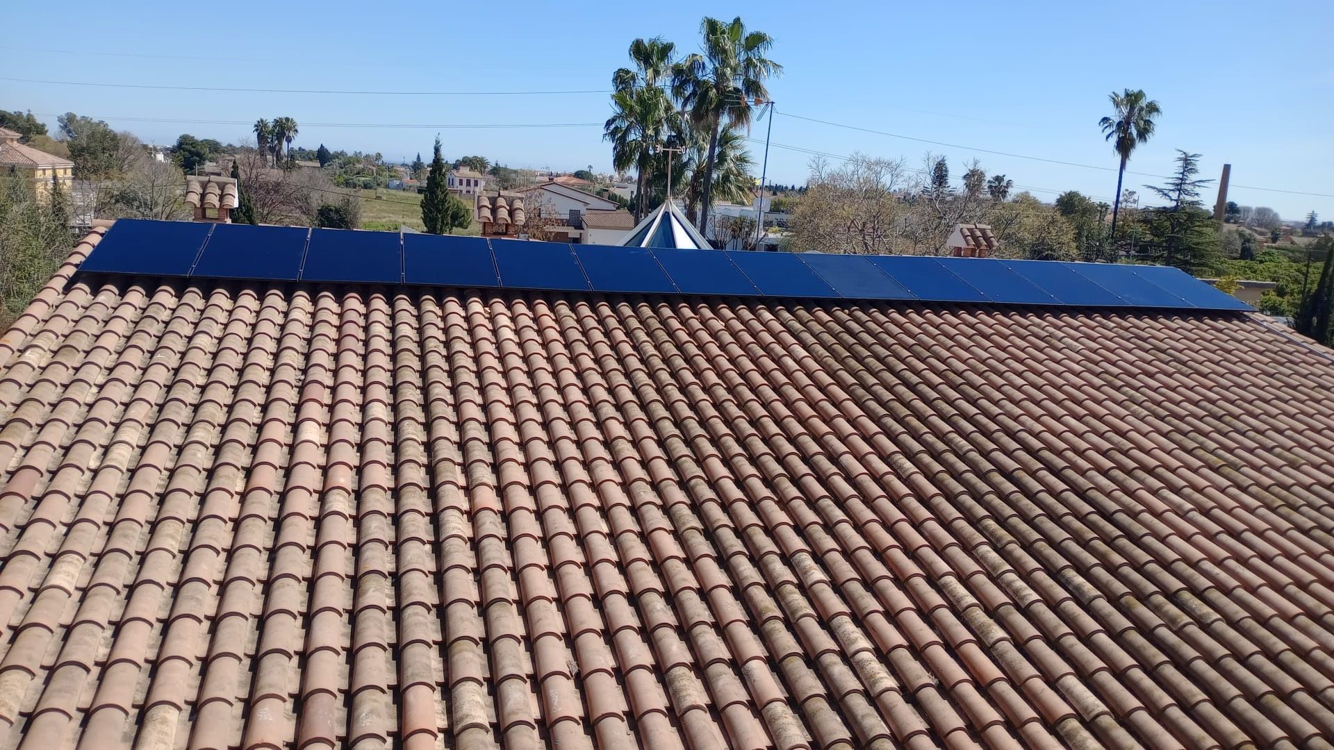 Paneles solares instalados en un techo de tejas, fondo de cielo azul.