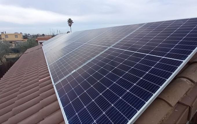 Paneles solares instalados en un techo de tejas marrones, en ángulo contra un cielo nublado.