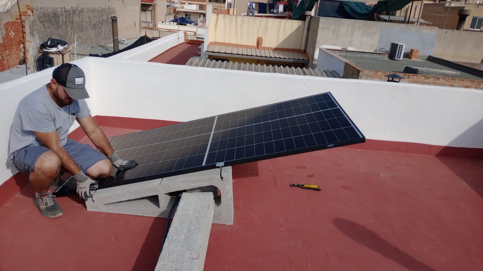 Hombre instalando un panel solar en un edificio con techo rojo, al aire libre.