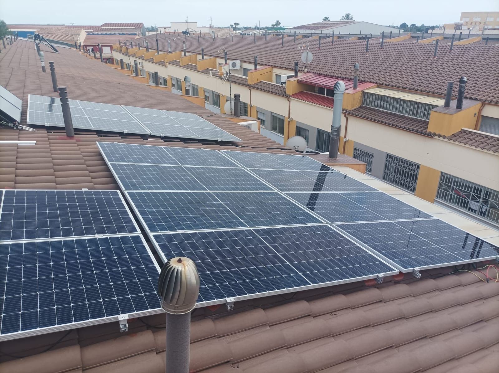 Paneles solares instalados sobre un tejado de tejas de terracota, con un barrio residencial visible al fondo.