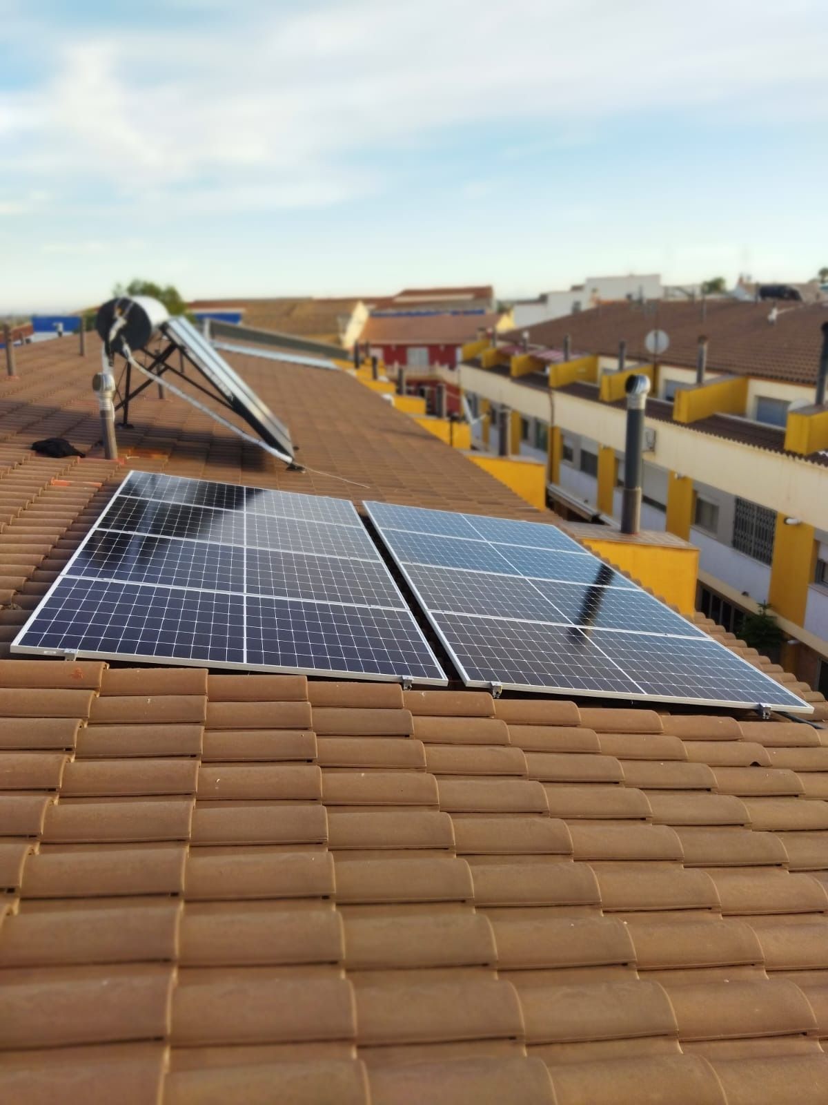 Paneles solares y un calentador de agua solar sobre un tejado de tejas de terracota, día soleado.