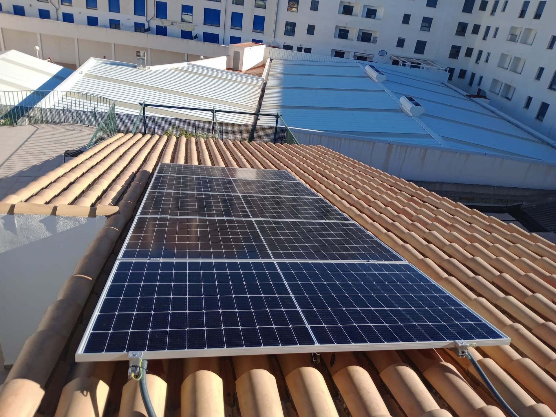 Panel solar sobre un tejado de tejas de terracota con otros tejados de edificios al fondo.