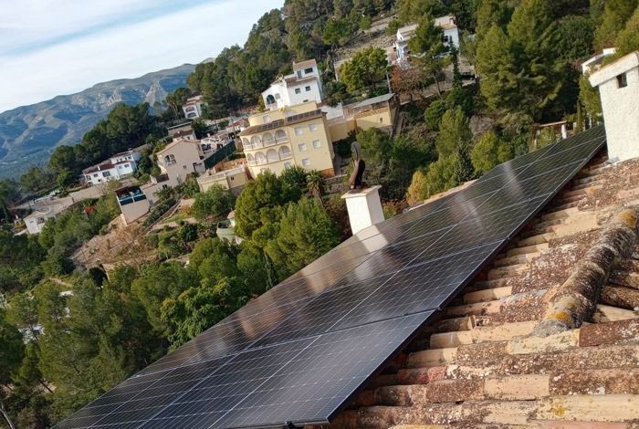 Paneles solares sobre un tejado de tejas de terracota con un pueblo en la ladera al fondo.