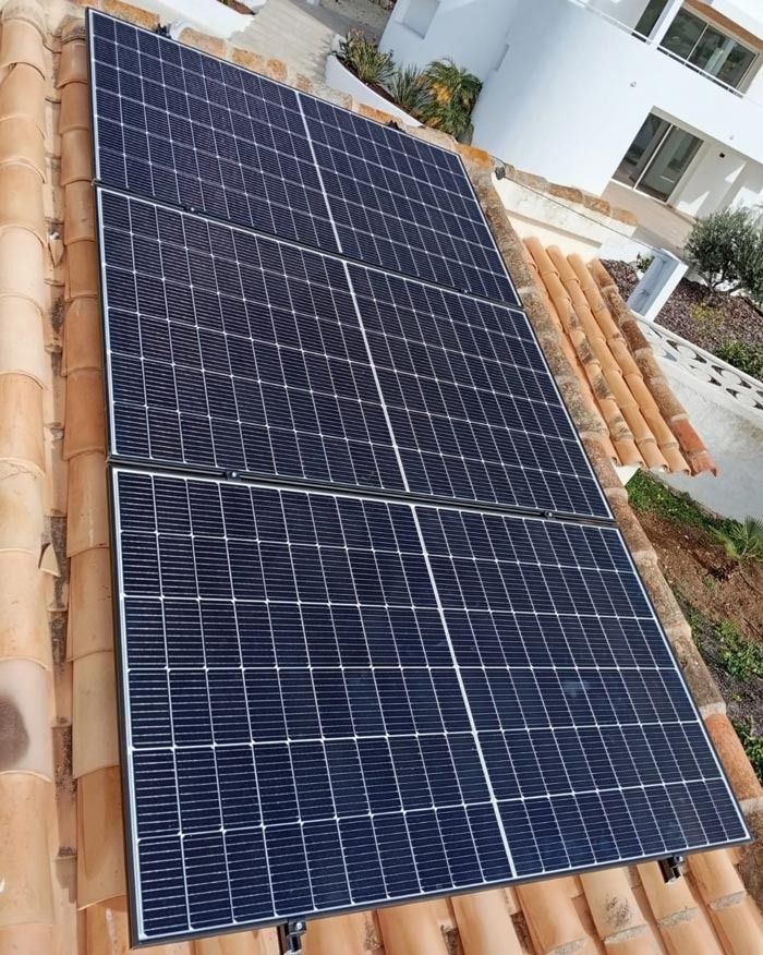 Paneles solares instalados en un techo de tejas de terracota de un edificio blanco, toma en ángulo.