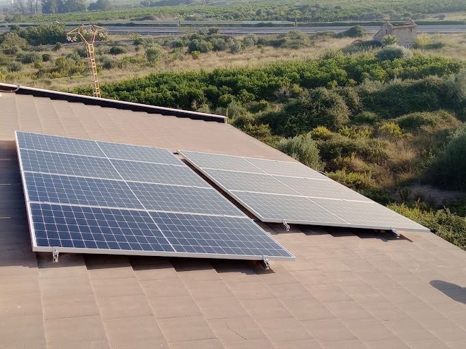 Paneles solares instalados en un techo de tejas marrones, con árboles verdes al fondo.