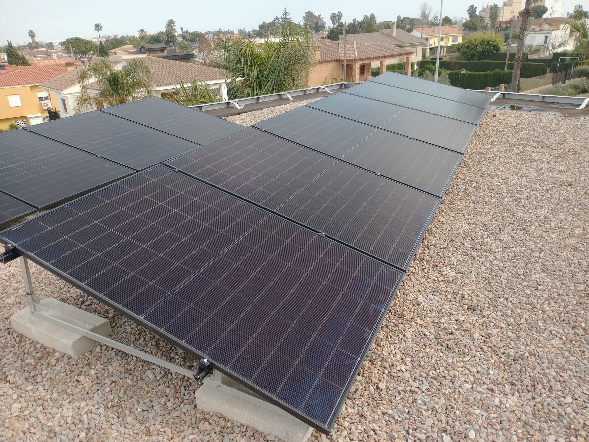 Paneles solares sobre un tejado de grava, orientados hacia el sol, con casas al fondo.