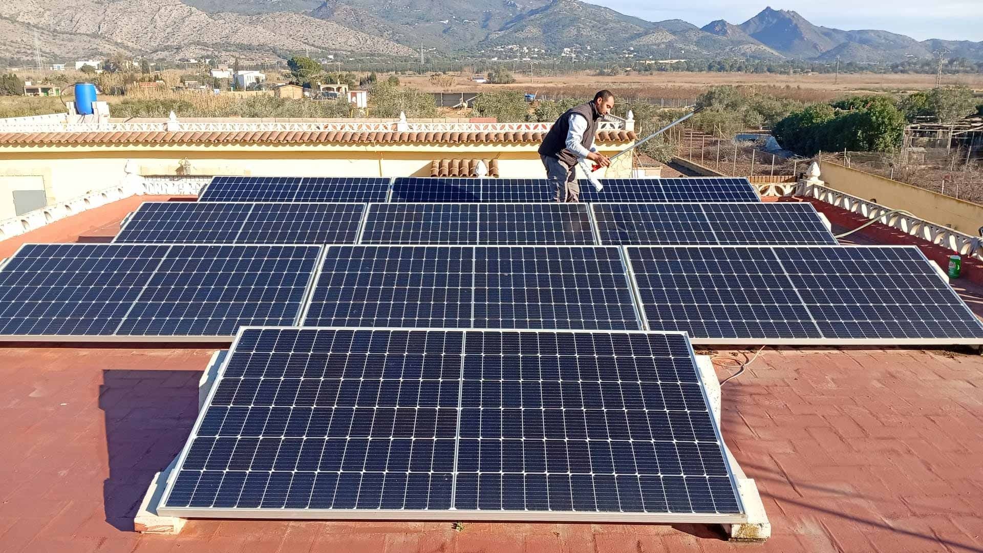 Hombre instalando paneles solares en un tejado de tejas rojas con vistas a la montaña de fondo.