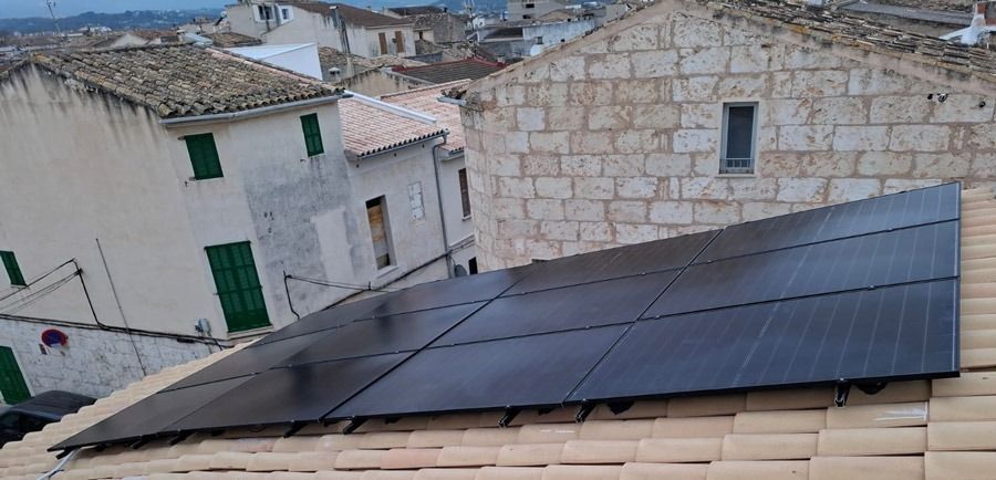 Paneles solares sobre un tejado de tejas en una ciudad. Se ven edificios al fondo.
