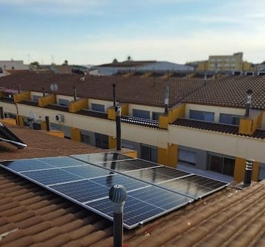 Paneles solares sobre un tejado de tejas en una zona residencial con edificios amarillos.