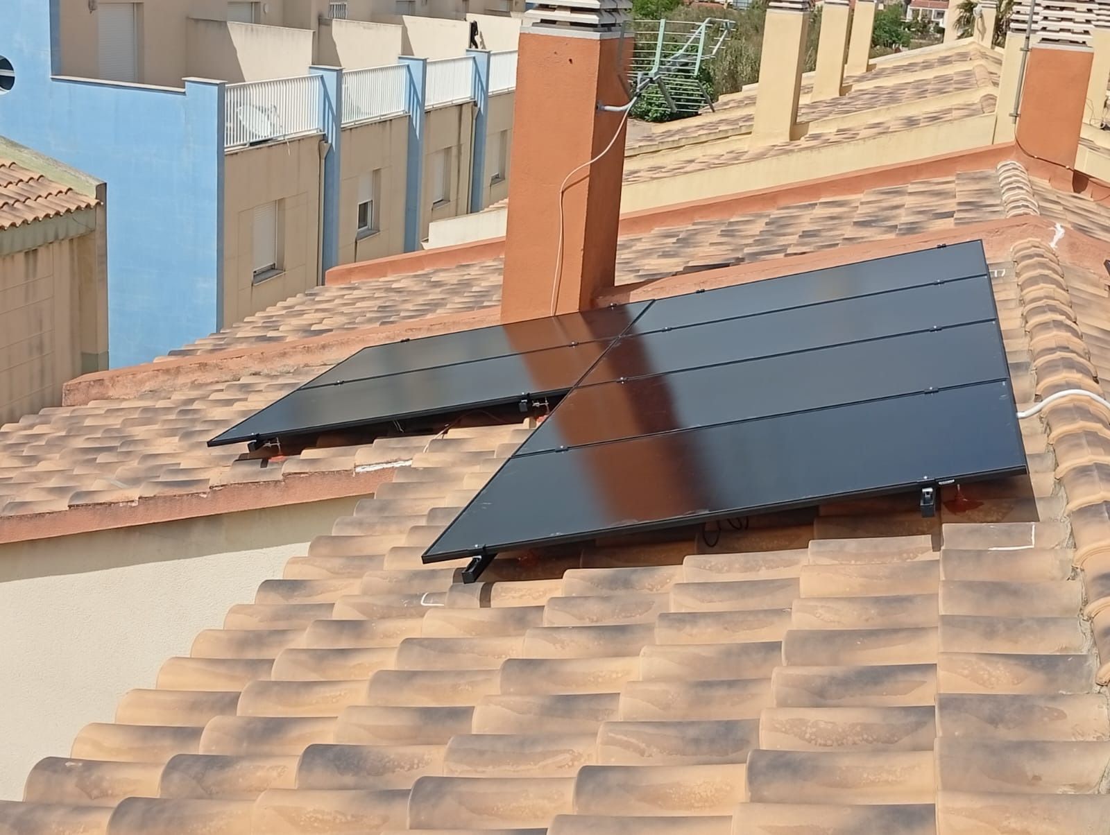 Paneles solares instalados en un tejado de tejas, cerca de una chimenea. Luz solar intensa.
