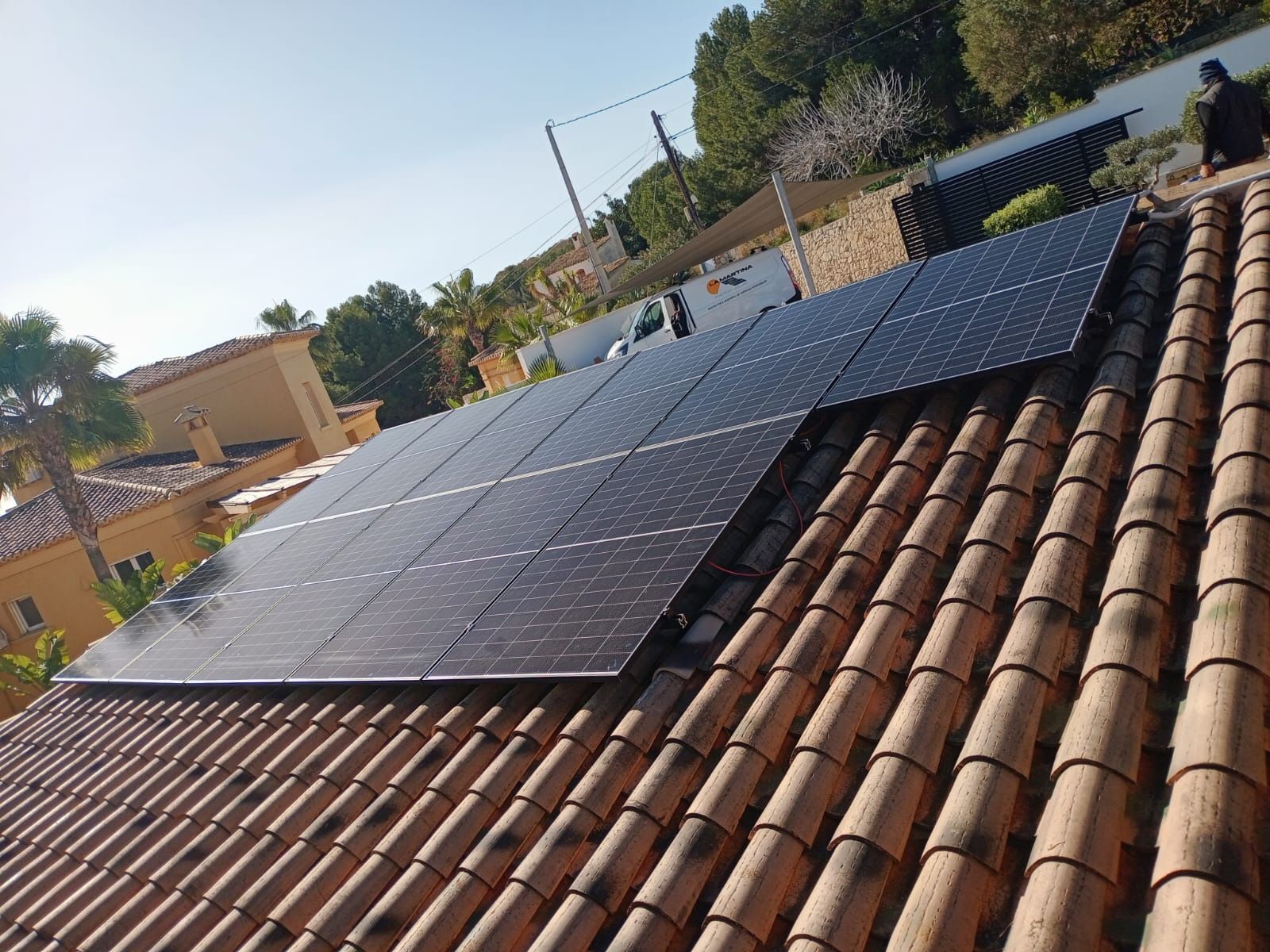 Paneles solares instalados en un techo de tejas de terracota, en un entorno exterior soleado.