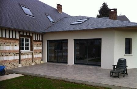 Vue extérieure d'une maison avec une façade en pierre et en bois, un toit en ardoise et une extension blanche moderne.