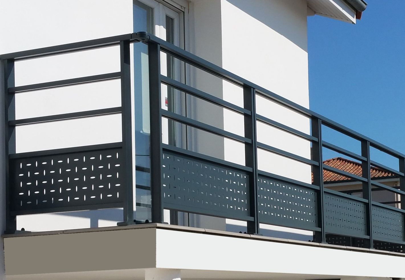 Rambarde de balcon en métal gris sur un bâtiment blanc, avec un ciel bleu en arrière-plan.