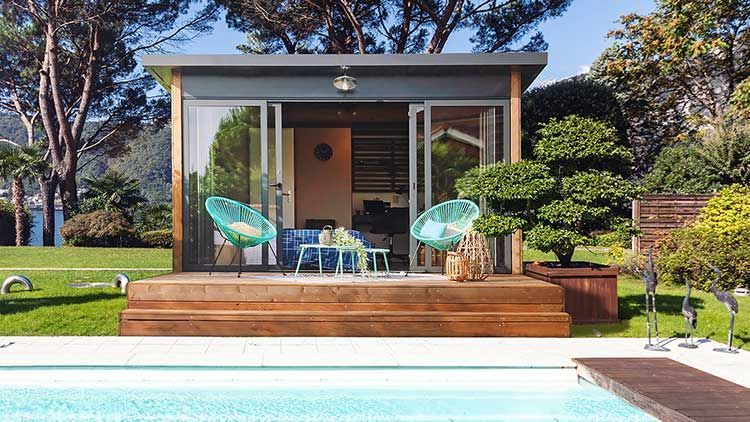 Cabane moderne en plein air avec terrasse, piscine et chaises turquoise, dans un cadre verdoyant luxuriant.