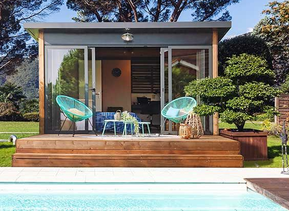 Des volets verts s'ouvrent à côté d'une fenêtre à cadre blanc sur un mur en stuc beige.
