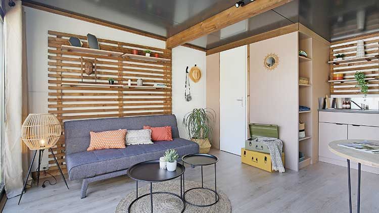 Salon cosy avec canapé gris, mur d'accent en bois, tables basses noires et murs rose clair.