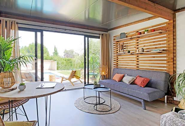 Maison à deux étages avec un toit de tuiles brunes et un auvent blanc. Murs beiges, volets foncés et petit balcon.