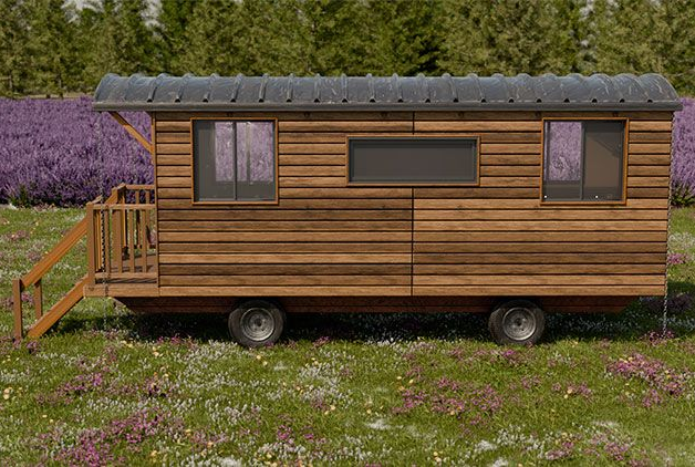 Cabane en bois sur roues avec deux fenêtres, un petit porche et un toit en métal. Située dans un champ de fleurs.