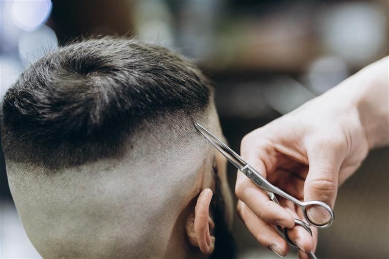 Un barbero cortando el cabello de un hombre con tijeras, primer plano de la cabeza.