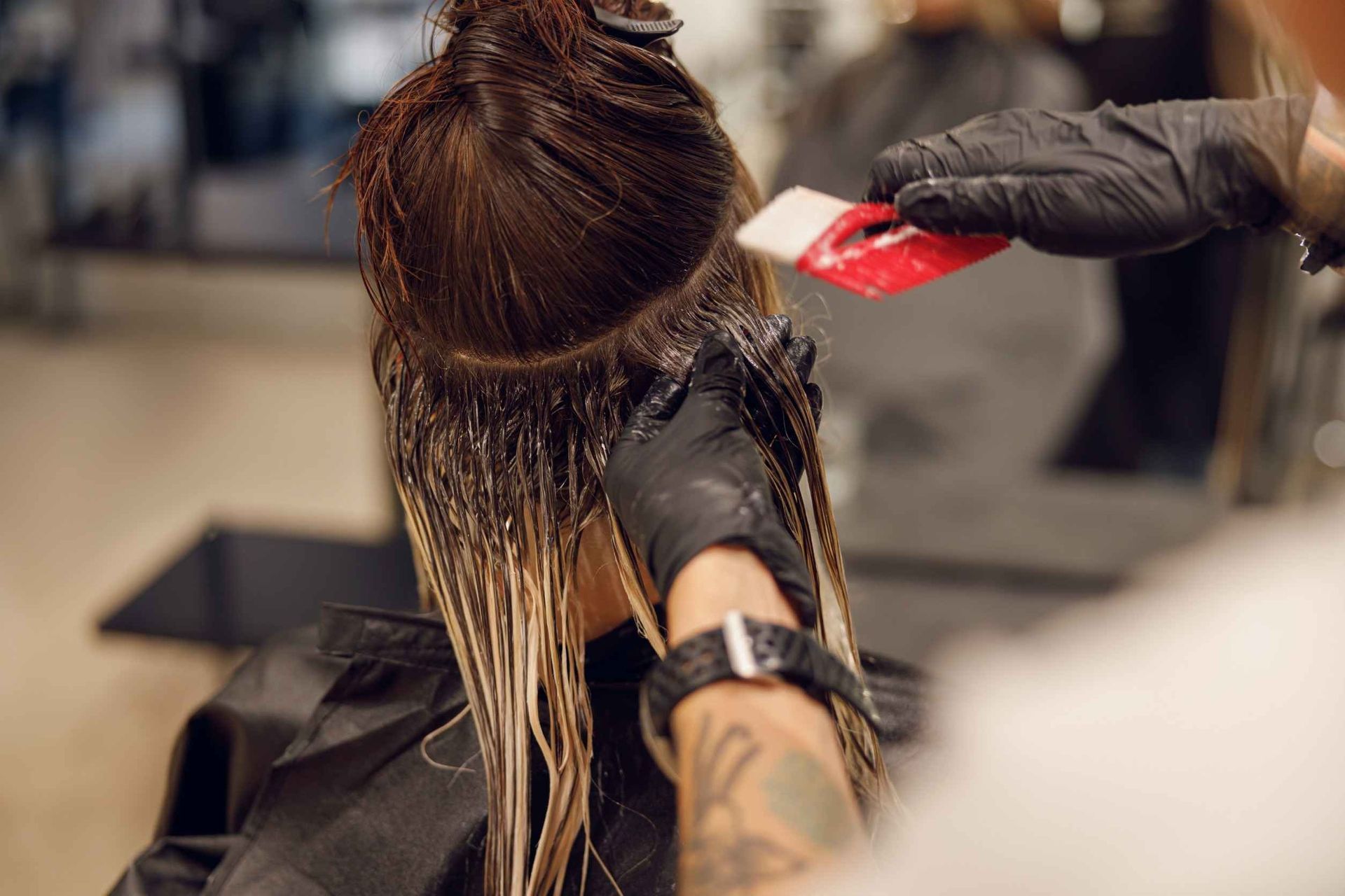 Una persona recibe tinte para el cabello aplicado por un estilista con guantes negros en un salón.