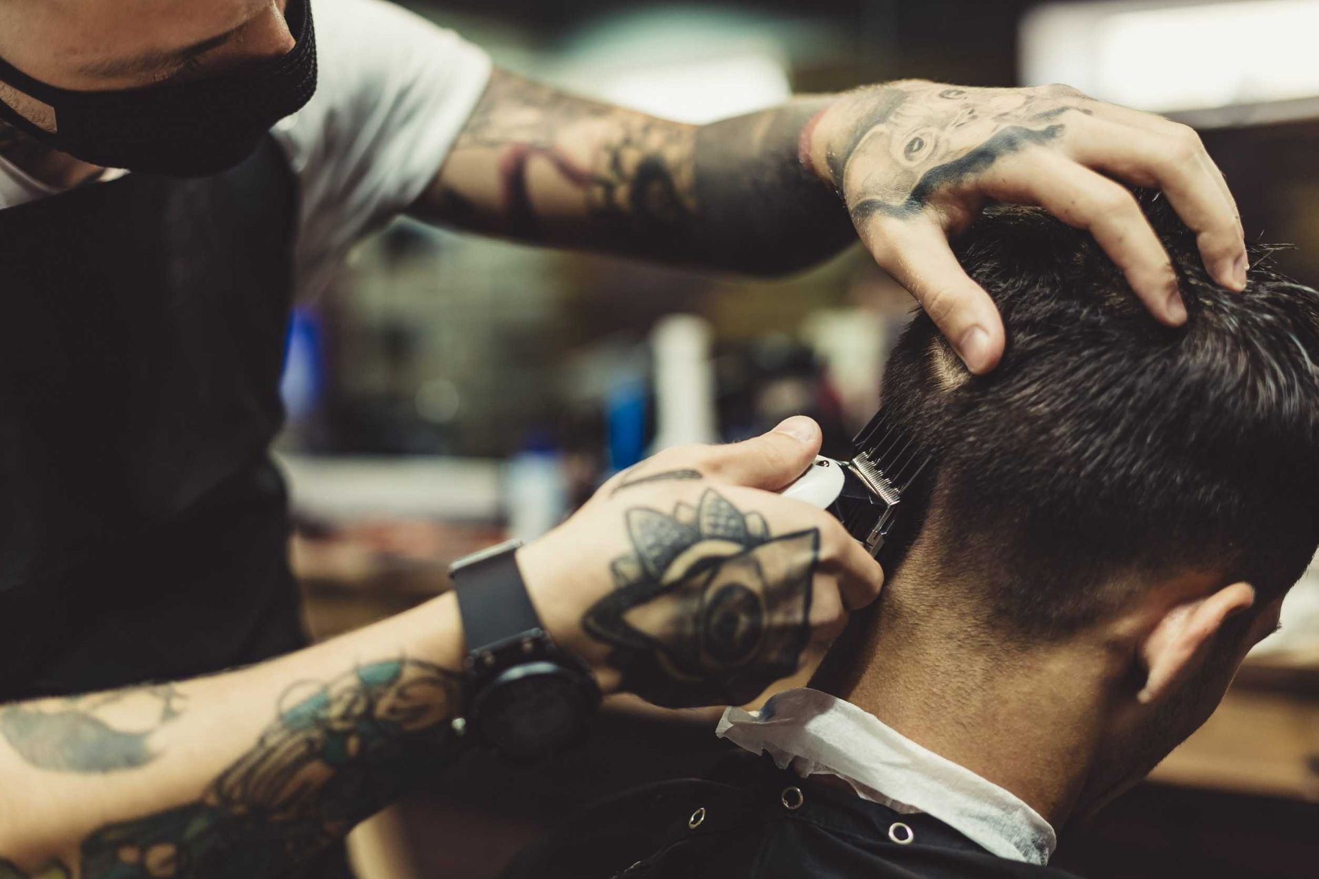 Barbero con tatuajes cortando el pelo a un hombre con una maquinilla.