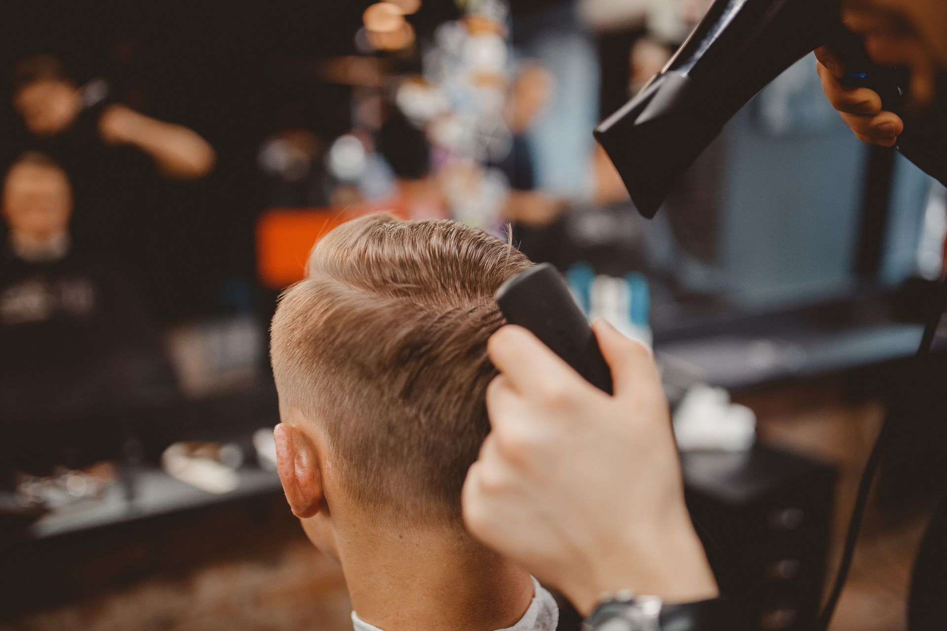 Hombre cortándose el pelo, estilista usando secador de pelo y maquinilla en la peluquería.