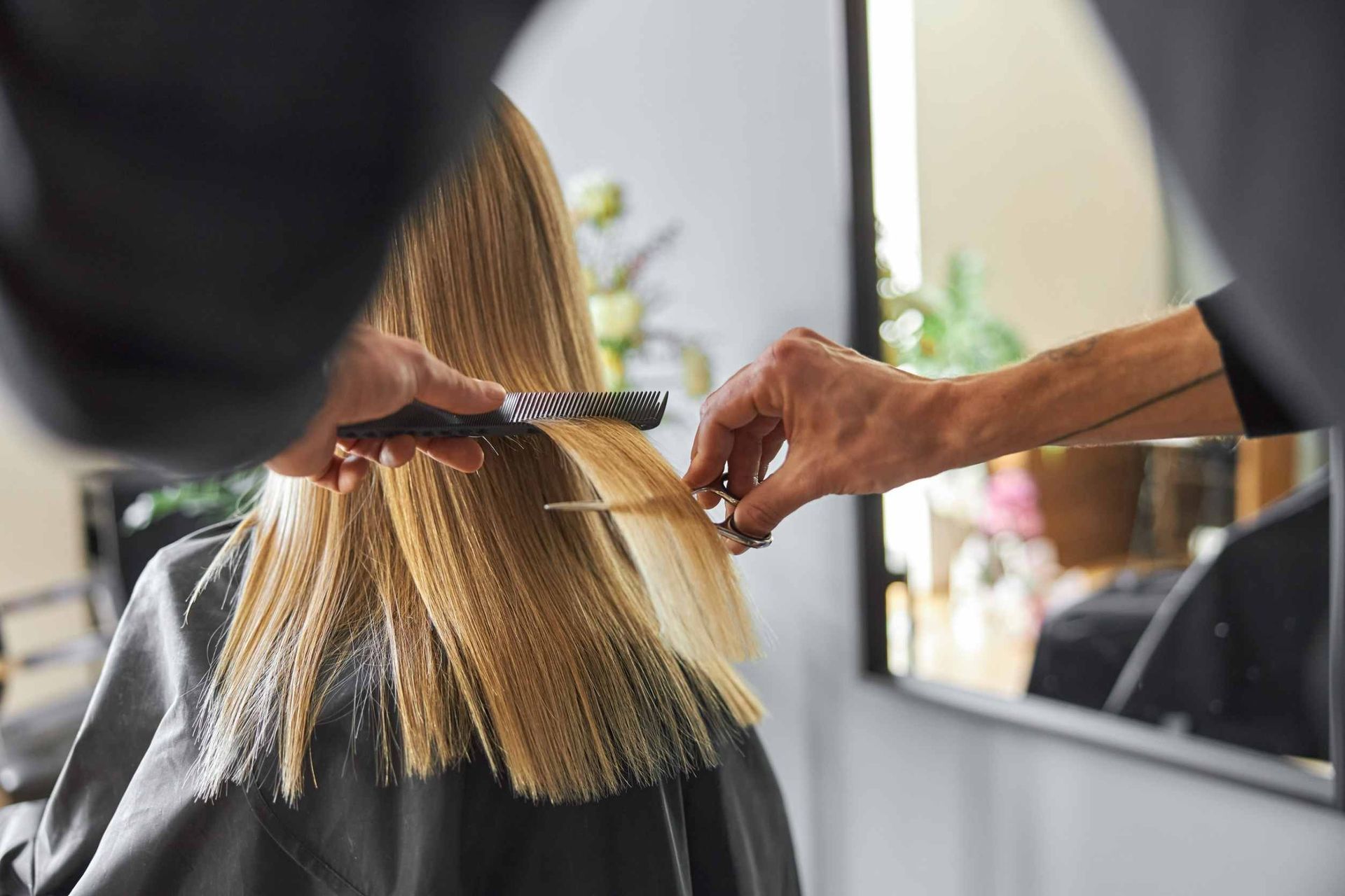 Peluquero cortando el cabello liso y rubio de una clienta en un salón.