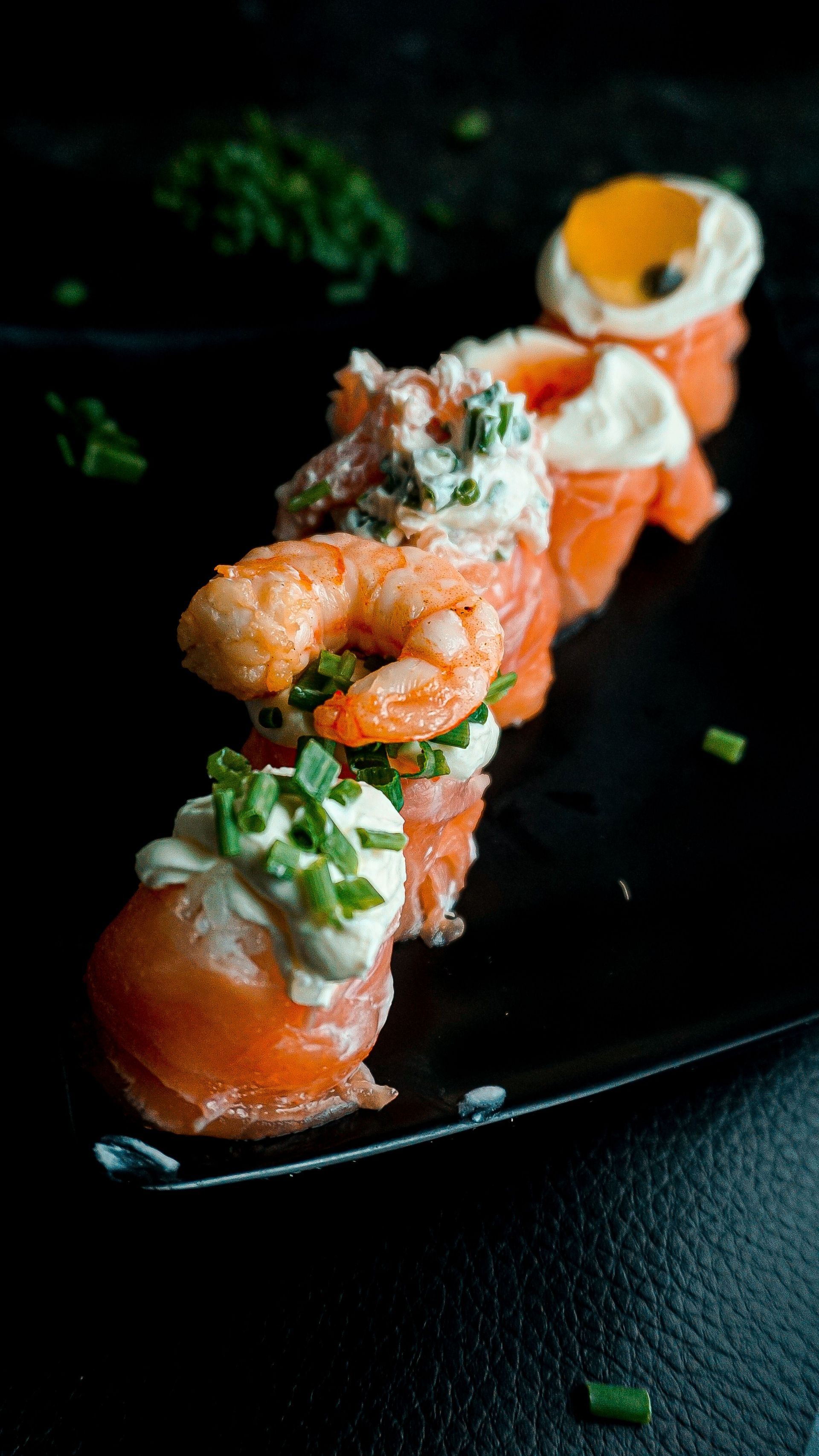 Rouleaux de sushi garnis de crevettes et de garniture sur une assiette noire sur fond sombre
