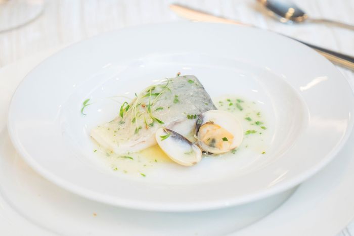 Plat de fruits de mer à l'assiette, nappé d'une sauce crémeuse et agrémenté d'herbes, sur une table blanche.